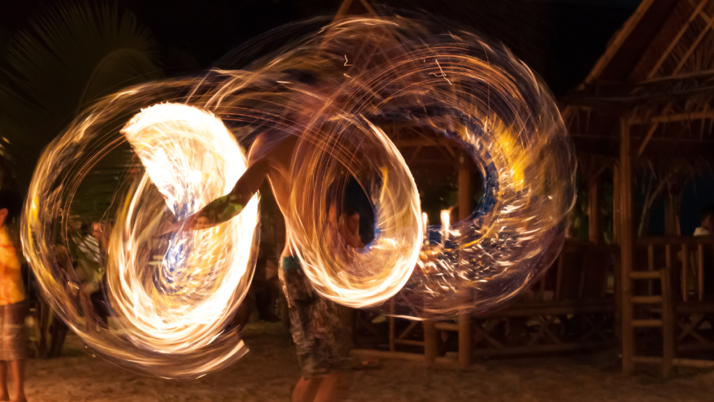 Long exposure photo of a fire dancer making shapes with flames around his body at night