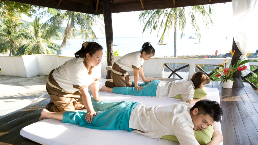 A couple receives a Thai massage treatment with palm trees and the Andaman Sea in the background